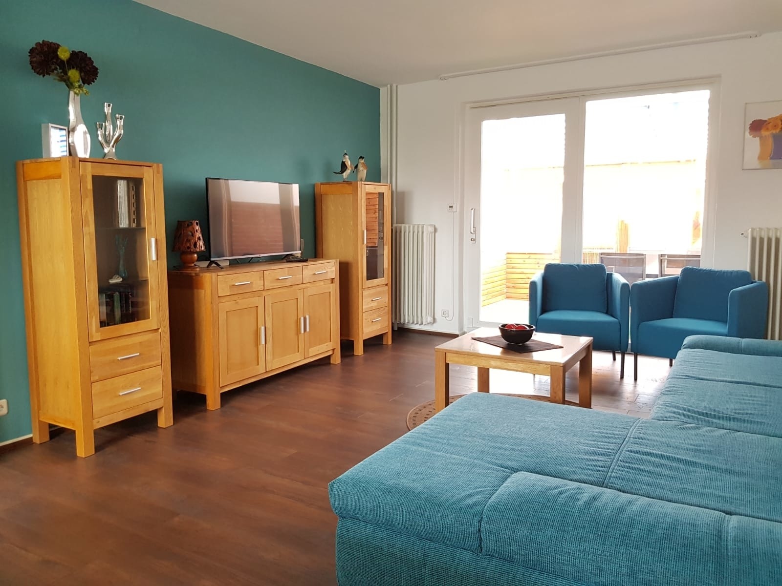 Helles Wohnzimmer mit türkisfarbenem Sofa und zwei Sesseln